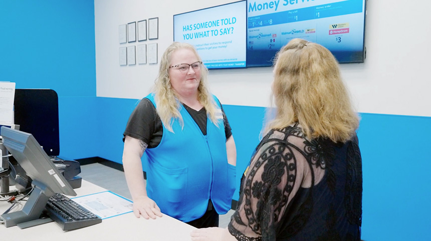 An associate in a blue vest talks with another person.