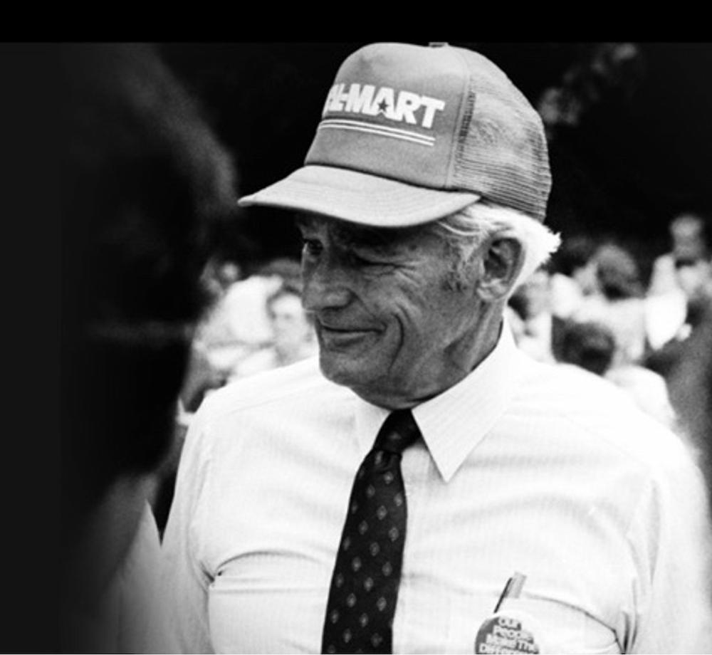 Sam Walton smiles while wearing a hat and tie